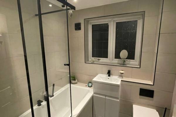 Photo of a new, white, modern bathroom that's been fitted in Southampton. Black glass shower dividers and a white sink and toilet.