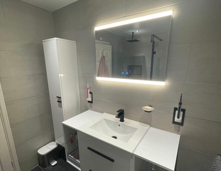Photo of a new, white, modern bathroom that's been fitted in Southampton. Light up mirror and white sink.
