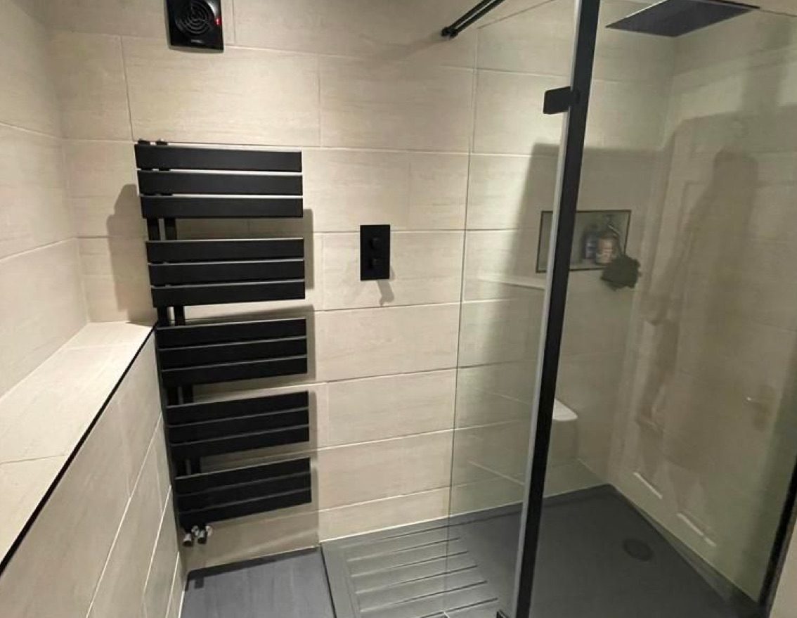 Photo of a new bathroom that's been fitted in Southampton. White tiles, black radiator, and glass shower dividers.