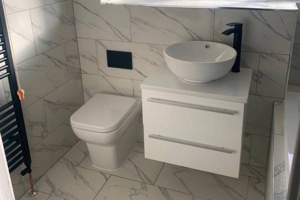 Photo of a white toilet and sink, installed on marble tiles, in a bathroom in Southampton.