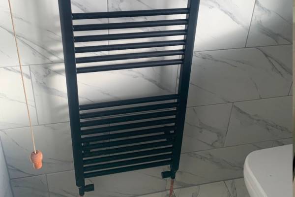 Photo of a black radiator mounted on marble tiles in a new bathroom fitted in Southampton.